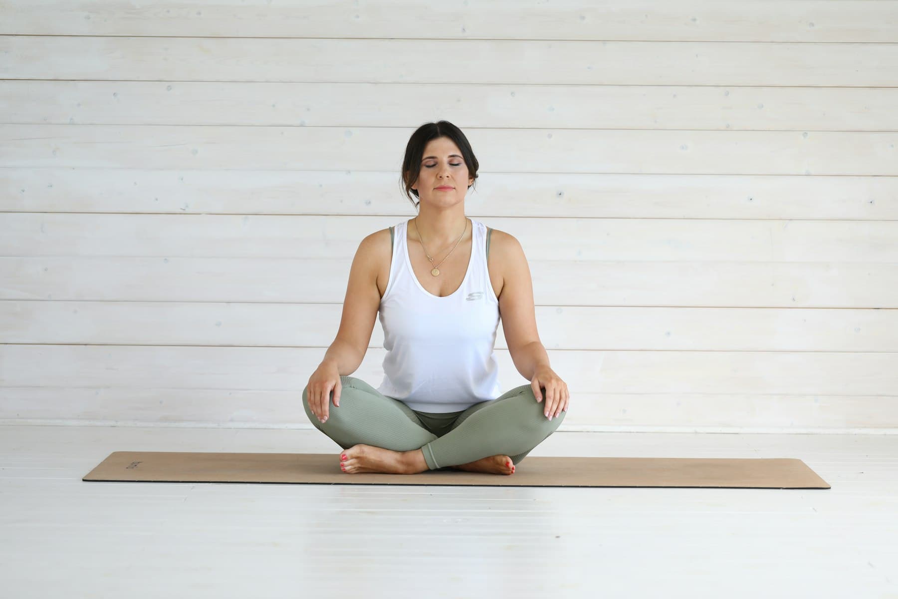 Frau sitzt ruhig und mit geschlossenen Augen auf einer Yogamatte — Pause statt Optimierung